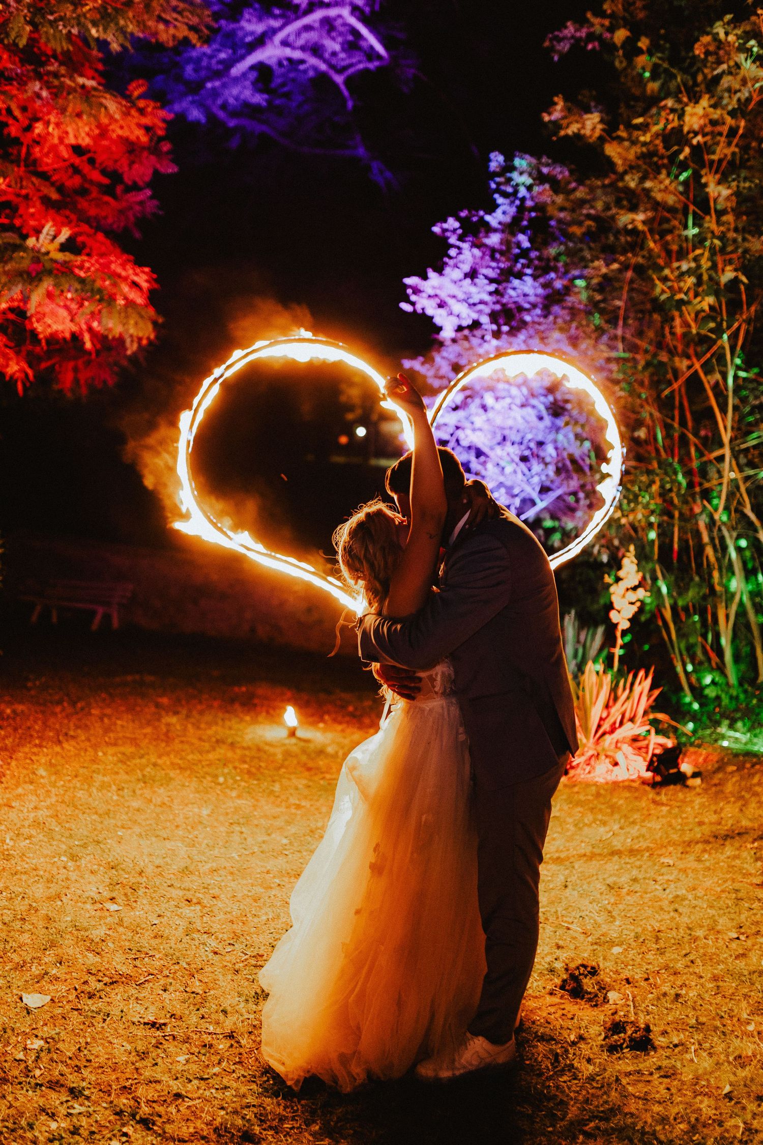 Wedding couple embraces under glowing heart-shaped light trails against colorfully lit foliage.