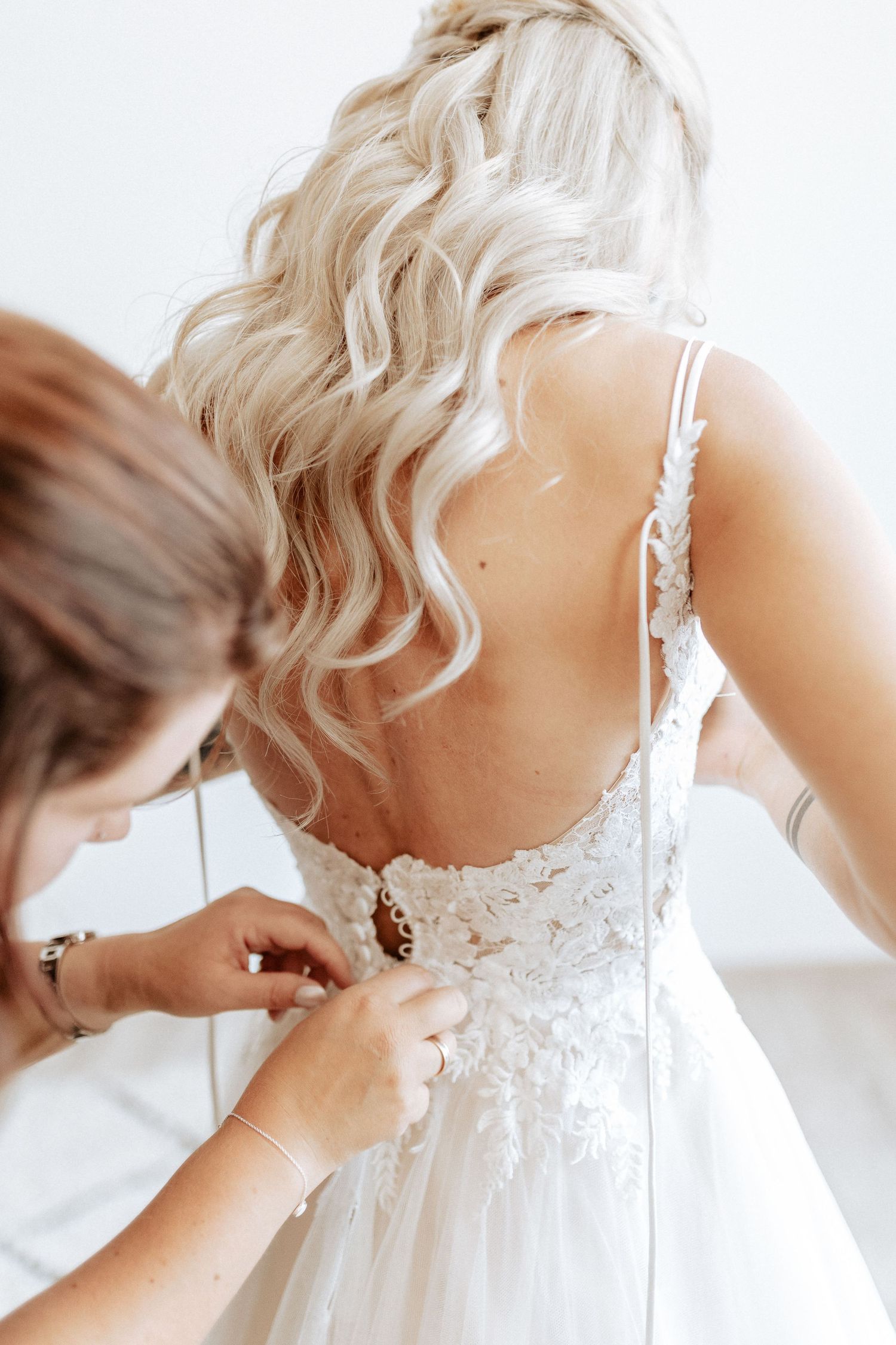 Close-up of intricate lace buttons being fastened on a white wedding dress.