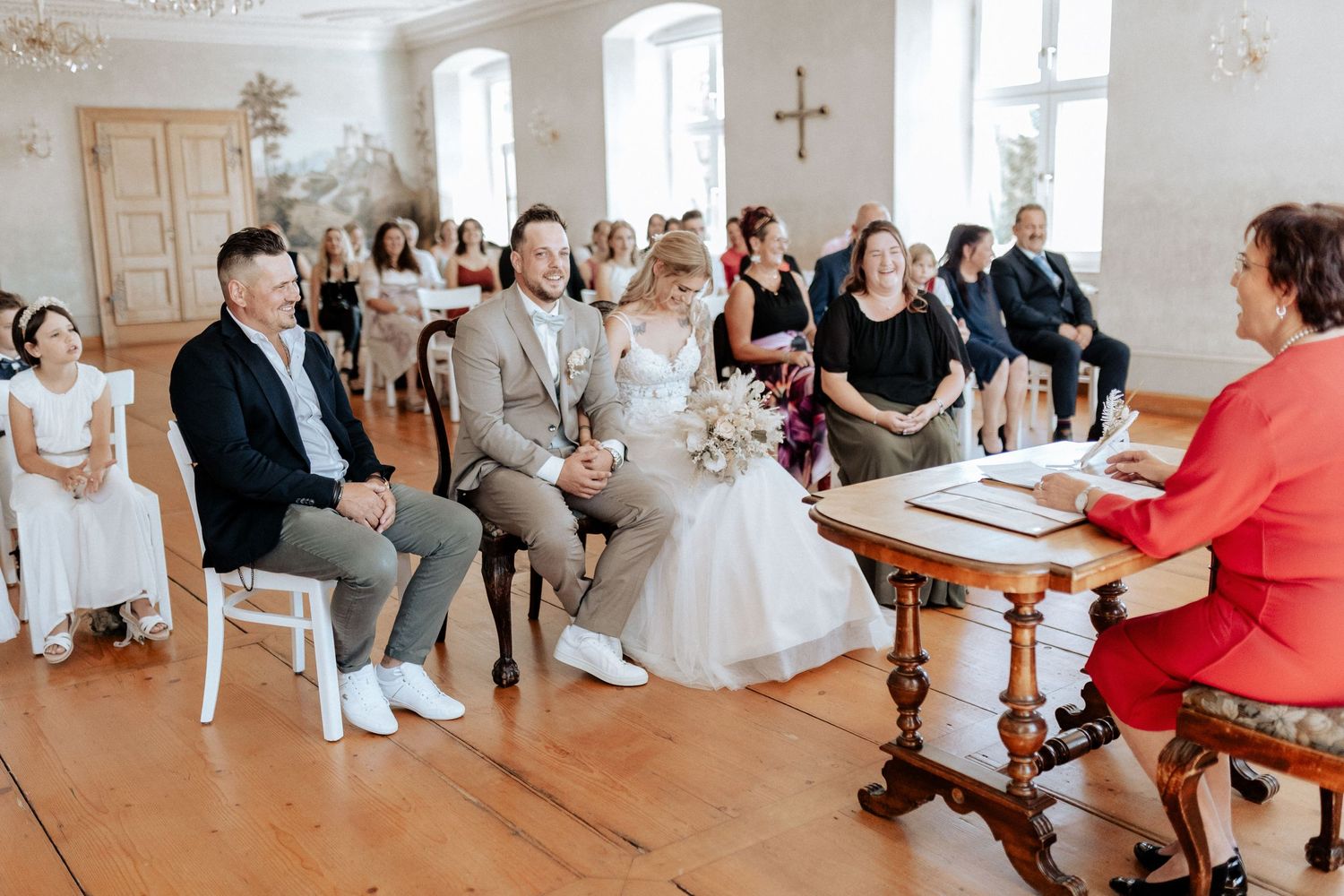An indoor civil ceremony with guests seated on white chairs in a bright traditional room.