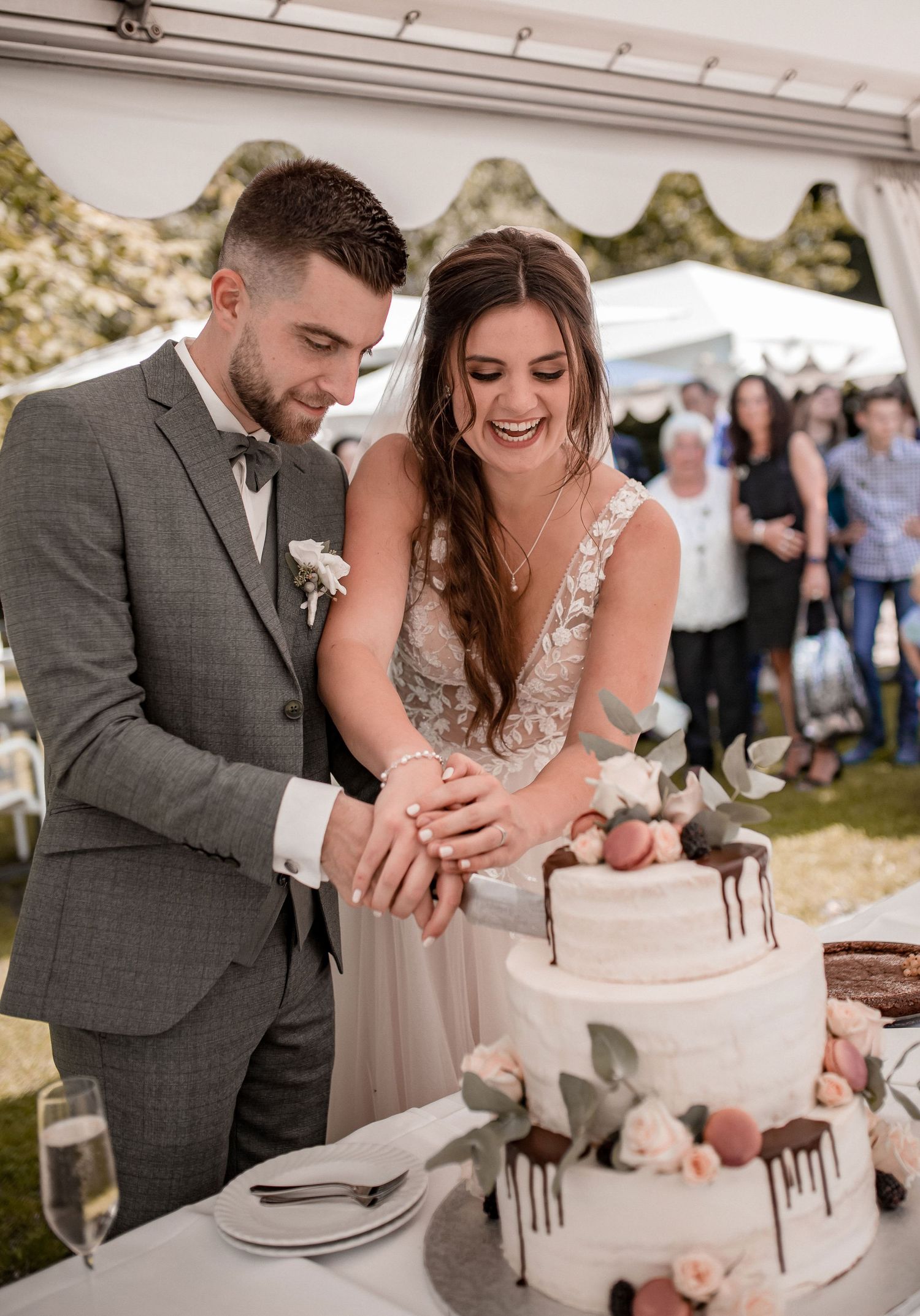 Newlyweds cut their elegant three-tiered white wedding cake under outdoor tent.