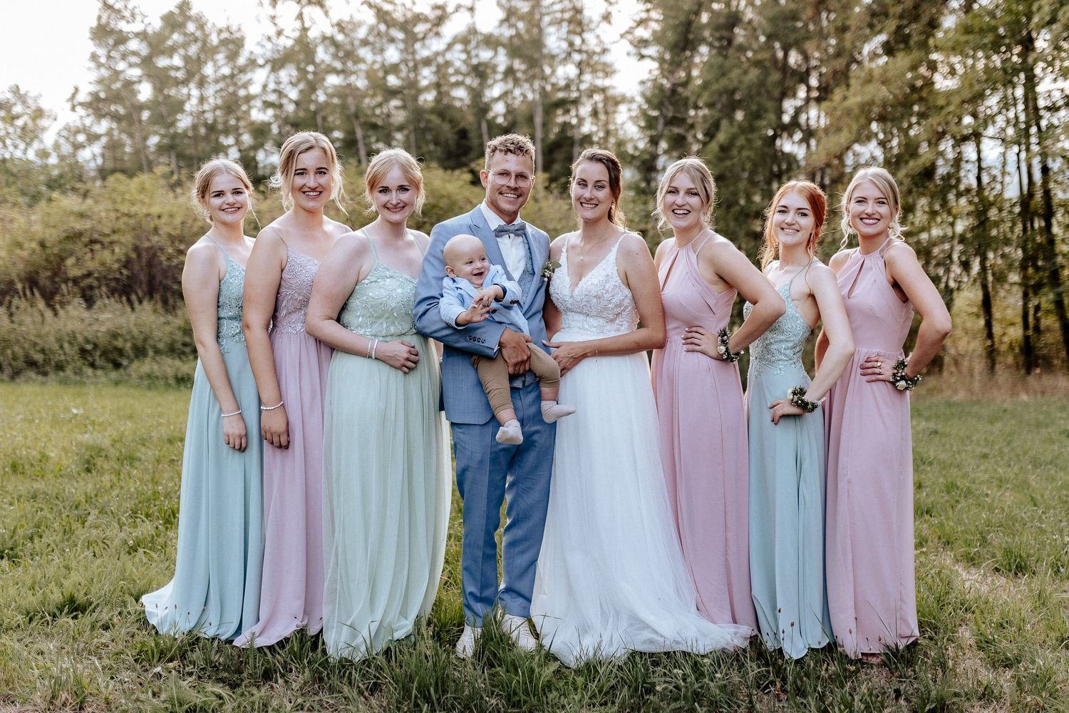 Wedding party poses outdoors in alternating pink and blue bridesmaid dresses.