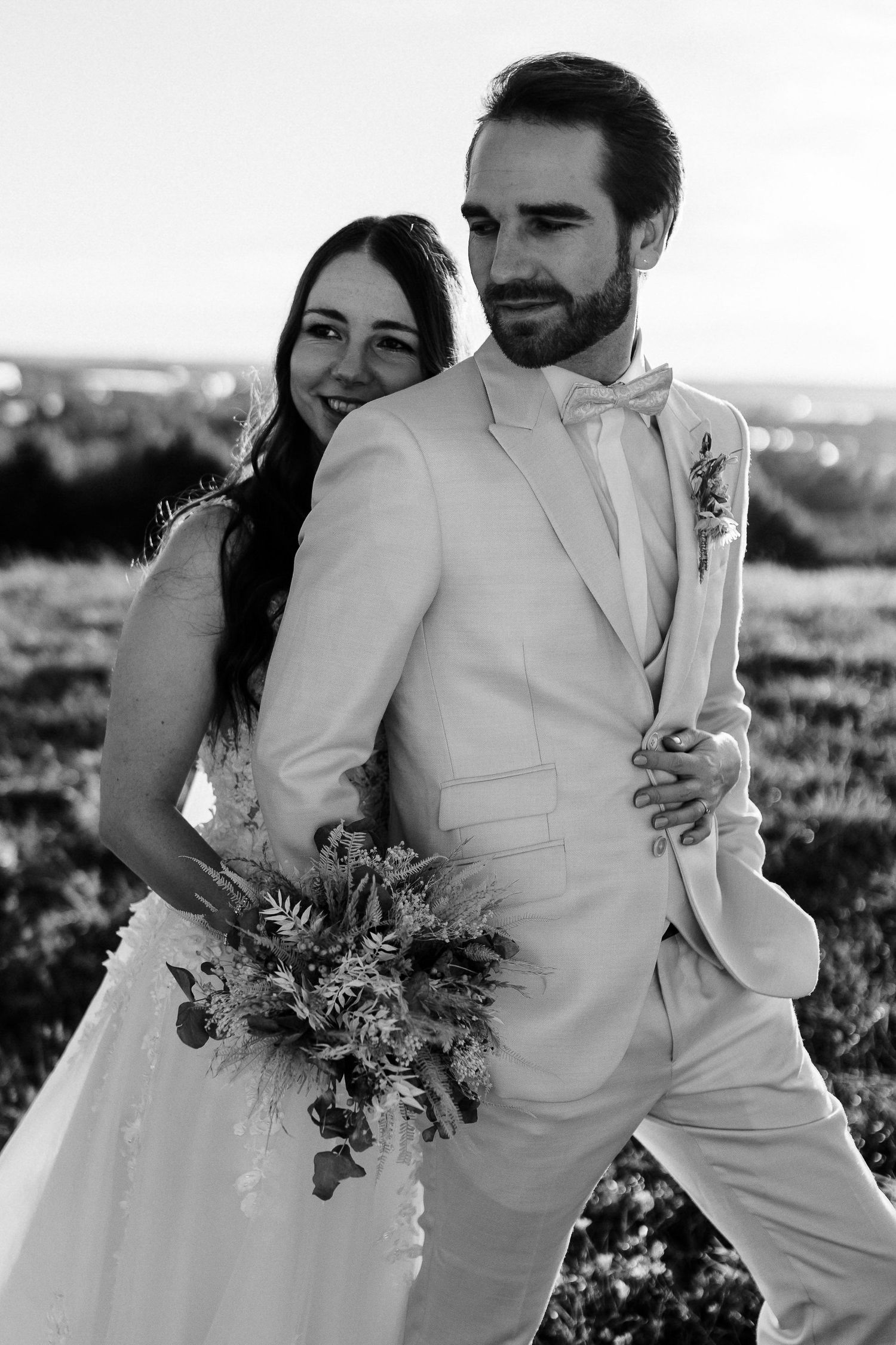 Black and white portrait of newlyweds embracing outdoors with scenic backdrop.