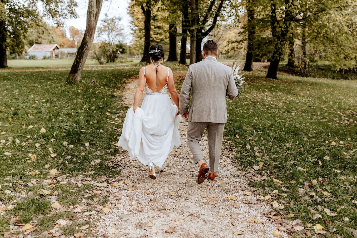 Couple walking away on autumn path surrounded by trees and fallen leaves.