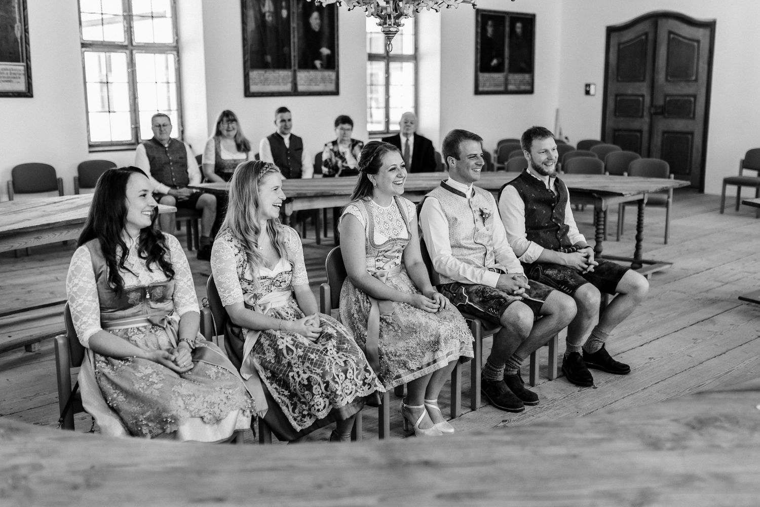 Wedding guests seated in traditional attire at a ceremony in a bright indoor venue.