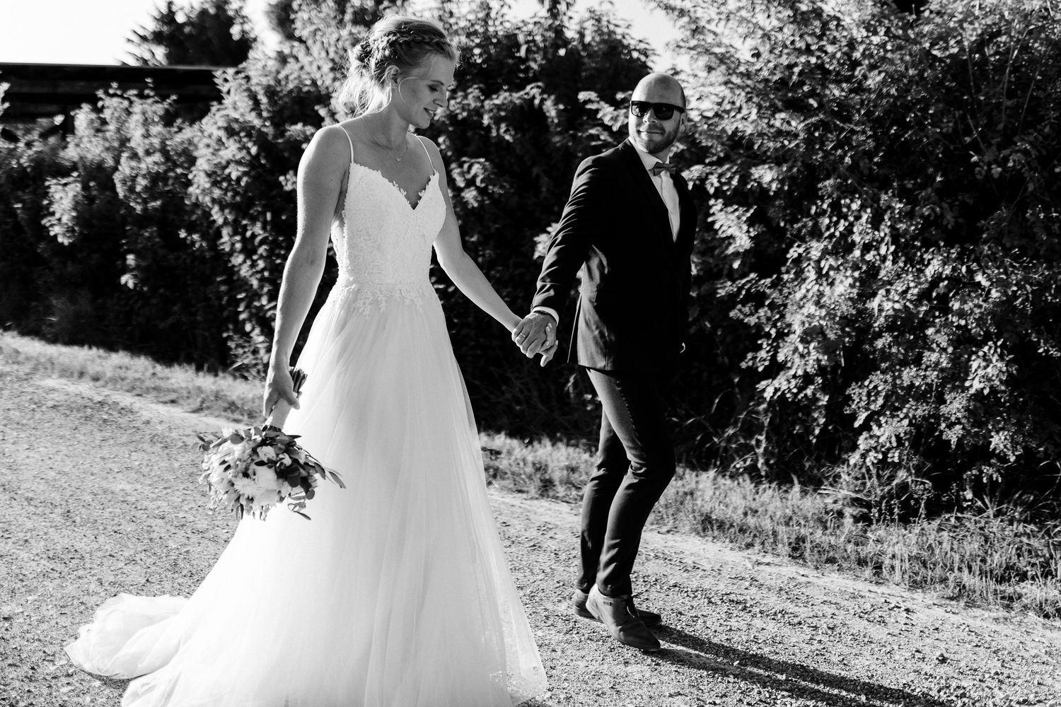Black and white photo of a bride in flowing gown walking with someone in a suit outdoors.