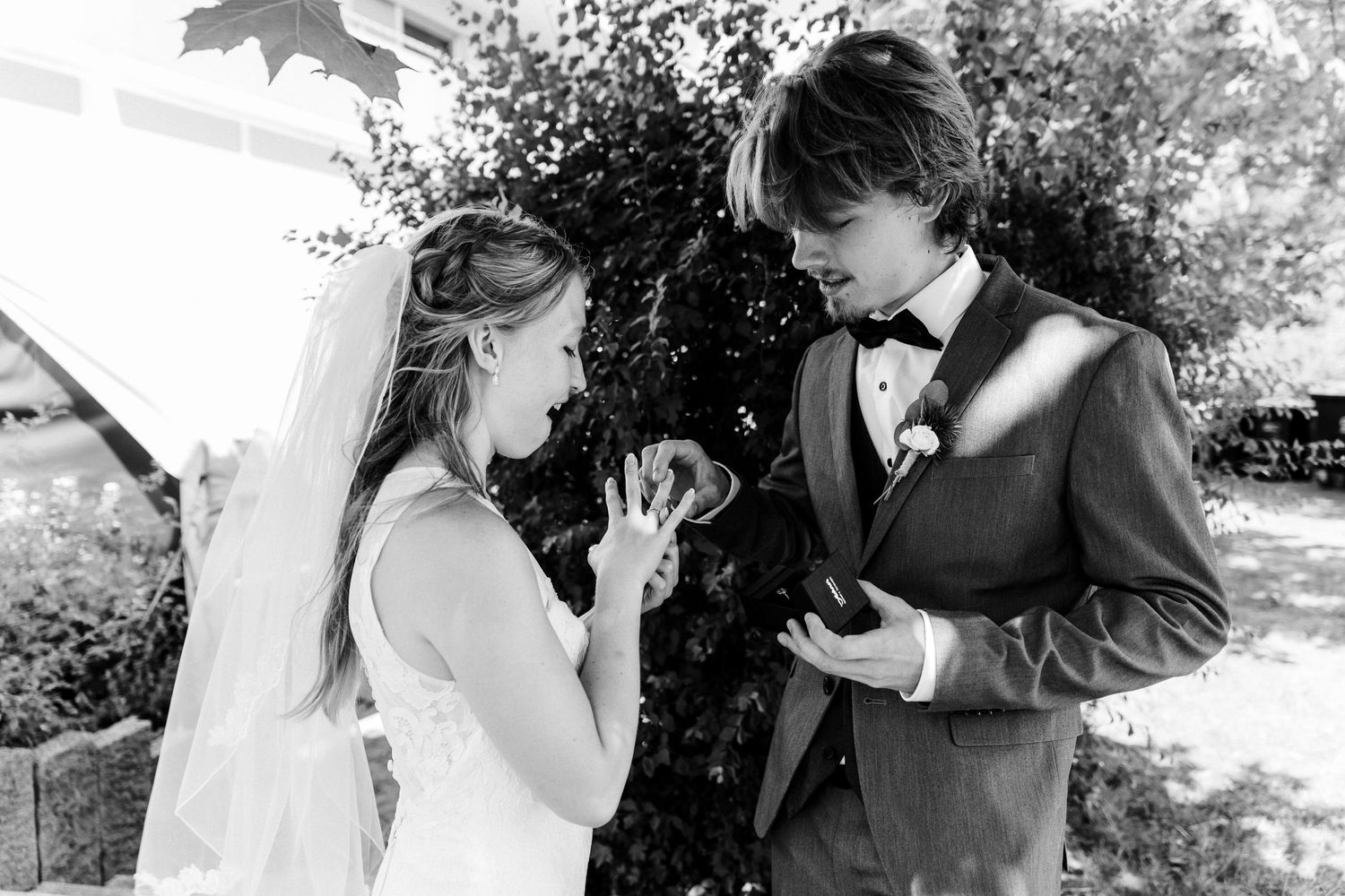 Black and white outdoor wedding photo showing an emotional moment between a couple exchanging rings.