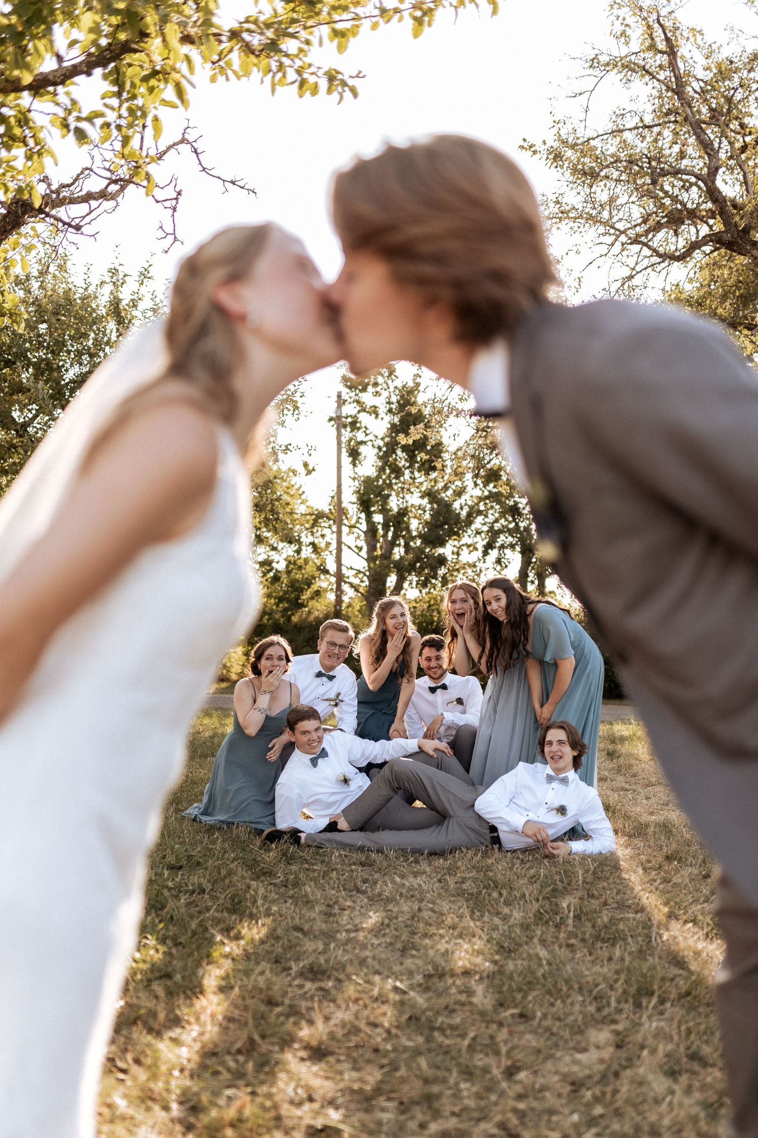 A creative wedding photo with guests gathered in the background while a couple shares a kiss.
