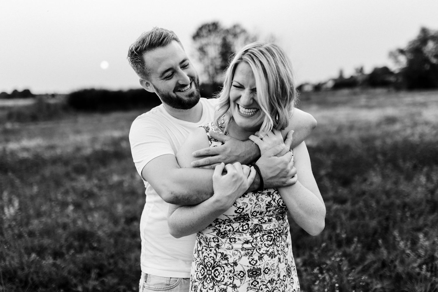 A joyful candid moment of laughter captured in black and white in a grassy outdoor field.