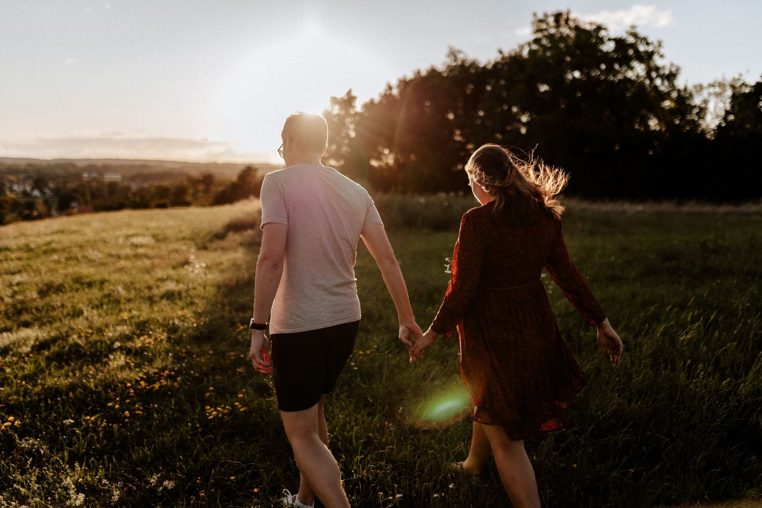 A couple walks hand in hand through a sun-drenched field at golden hour.