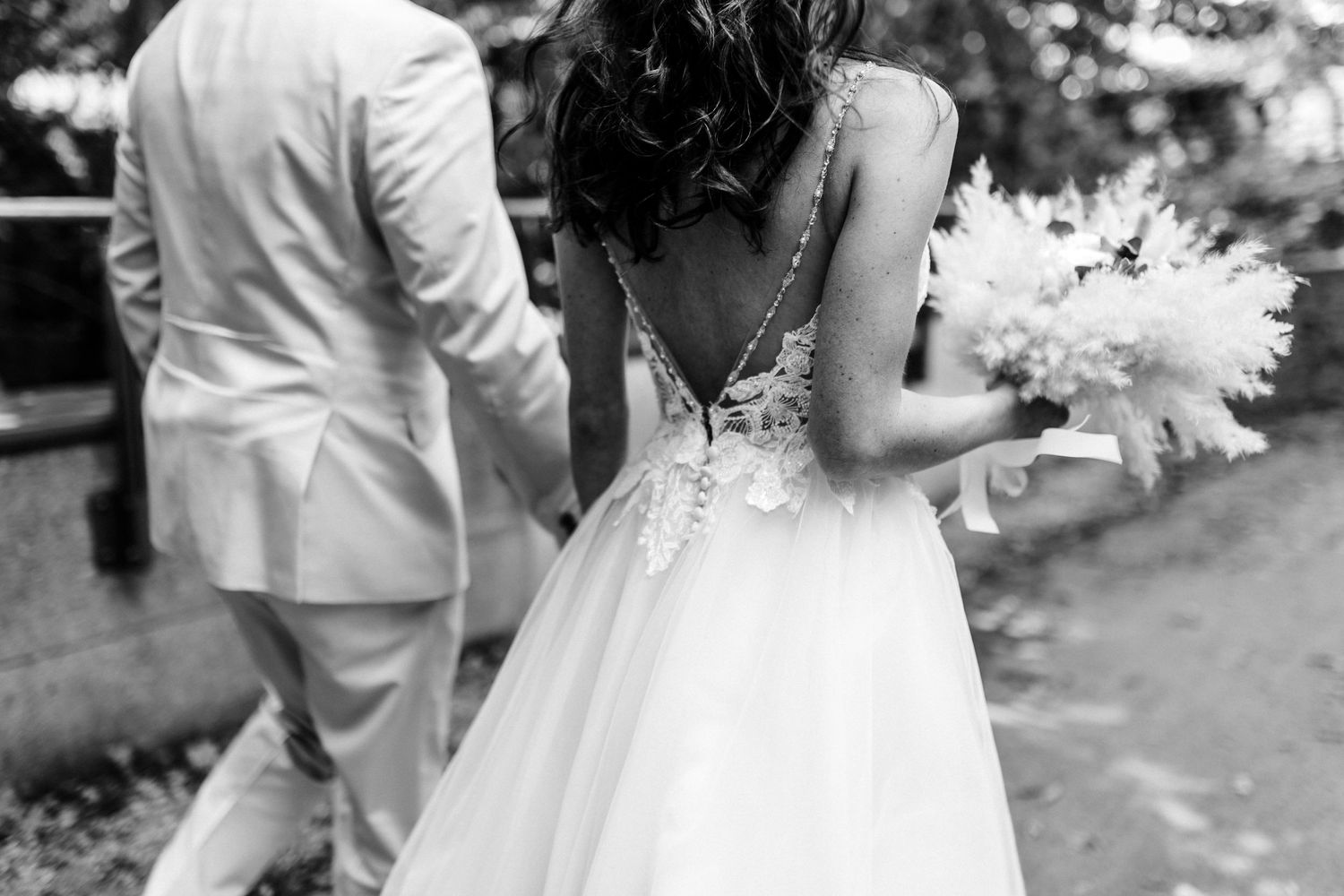 Black and white detail shot of bride's lace back wedding dress with white bouquet.