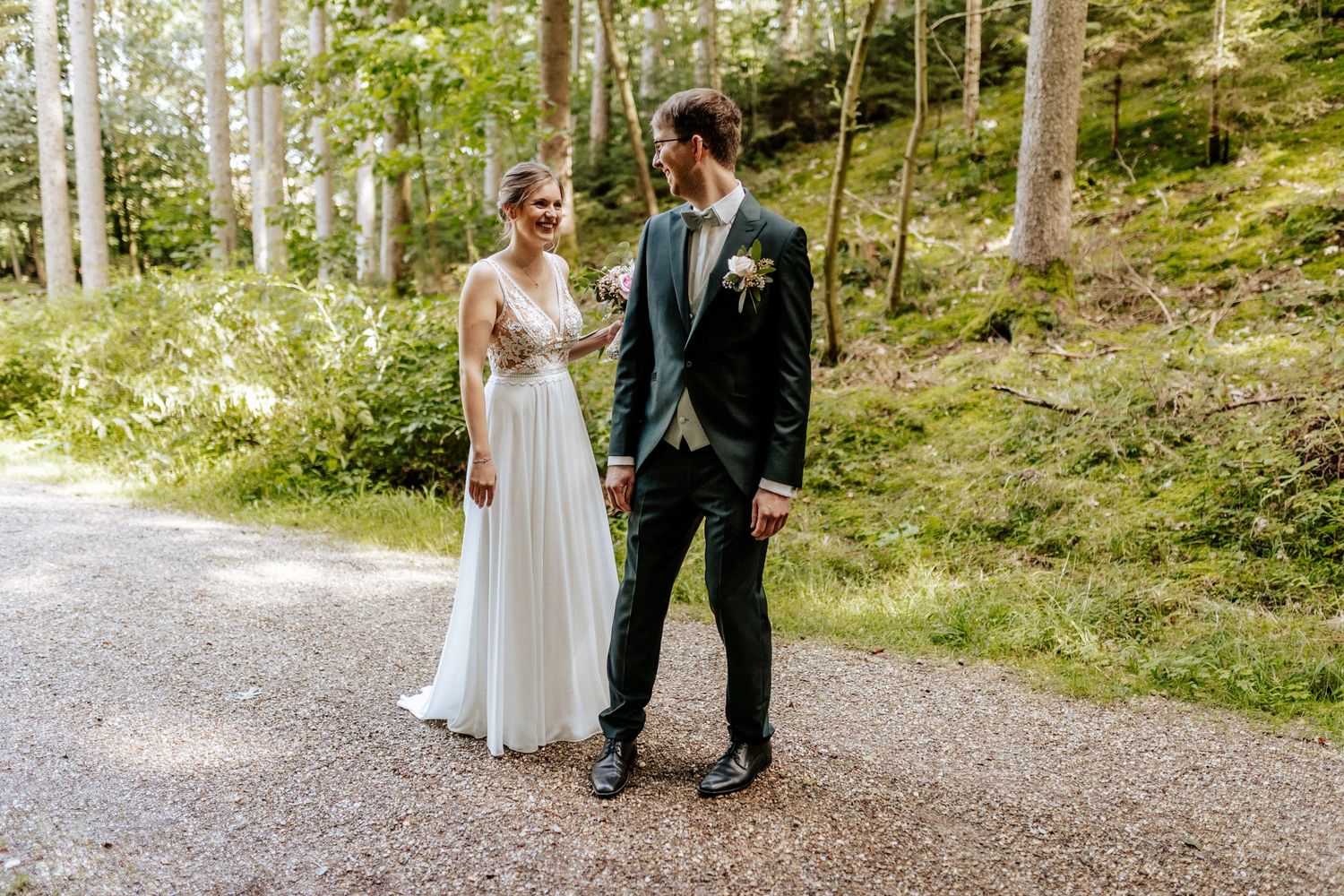 A couple shares a romantic moment on a forest path during their wedding photoshoot.