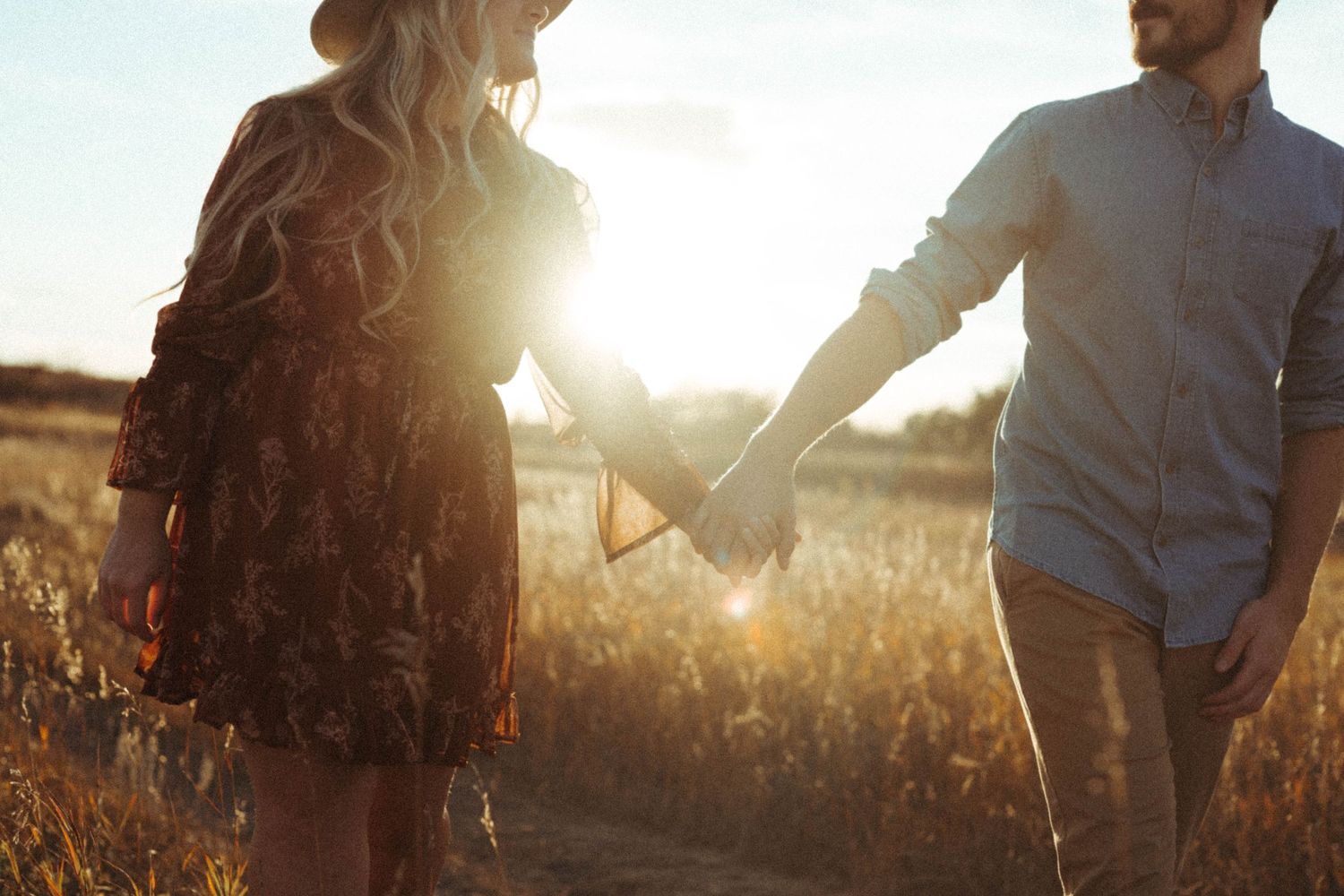 Silhouetted couple holding hands in golden sunlit field during sunset.