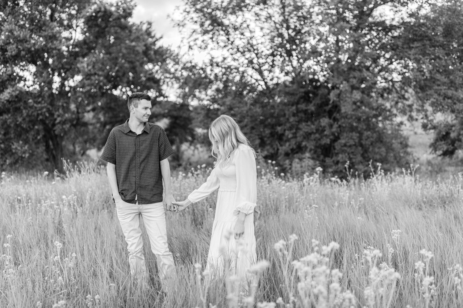 Couple holding hands and walking through tall grass in black and white photo.