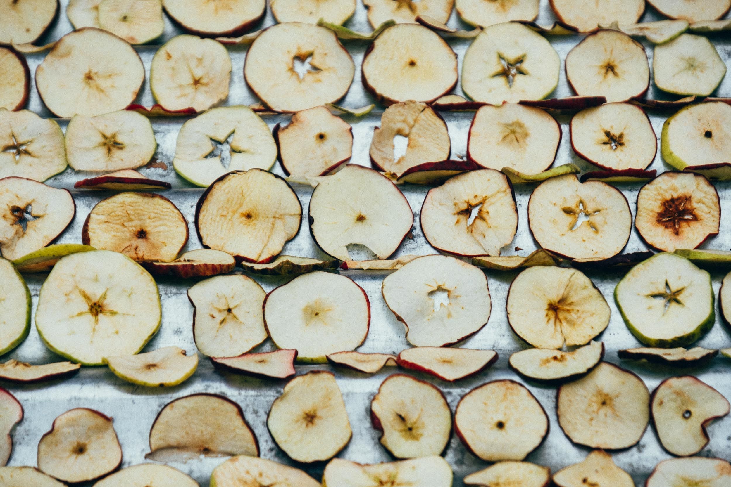 Rows of thinly sliced dehydrated apple rings laid out on a white surface showing their star-shaped cores.