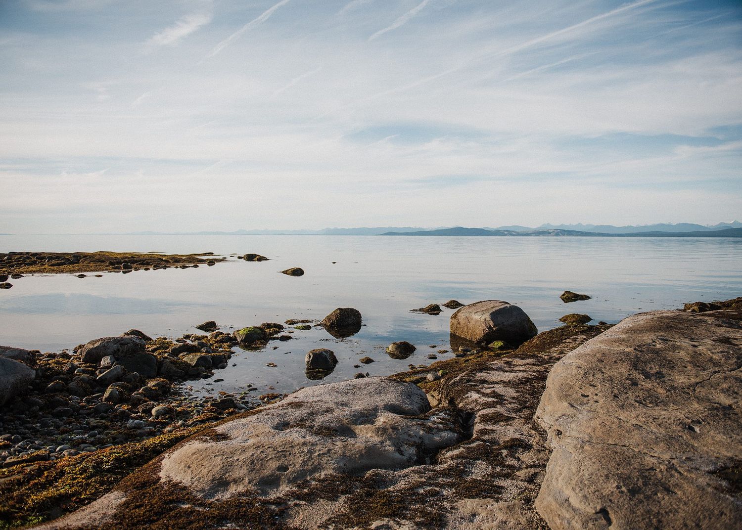 Tranquil seascape with scattered rocks and boulders along the shoreline under blue sky.