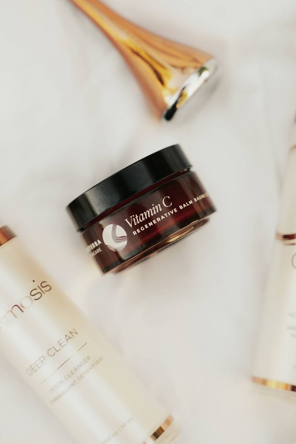 Premium skincare products including vitamin C cream and facial brush on white surface.