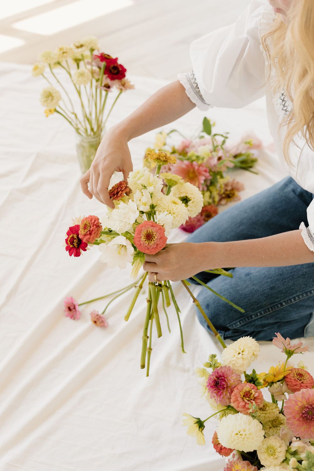 Arranging pink and white flowers into a bouquet on white surface.