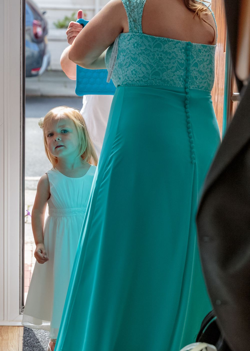 young flower girl peeps around the bridesmaid in the hallway at the brides parents house