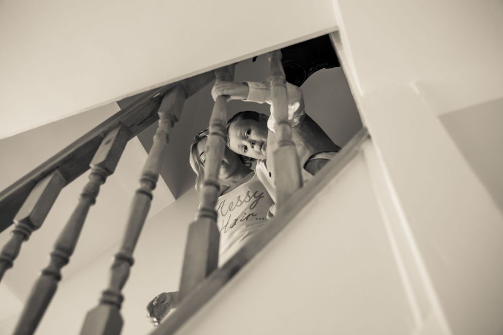 young boy sitting on the top of the stairs peeping through the rails