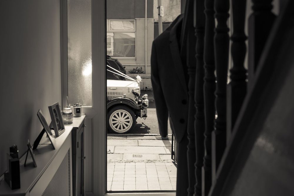 the front side of an old wedding car just visible through the open front door through the hallway at the brides parents
