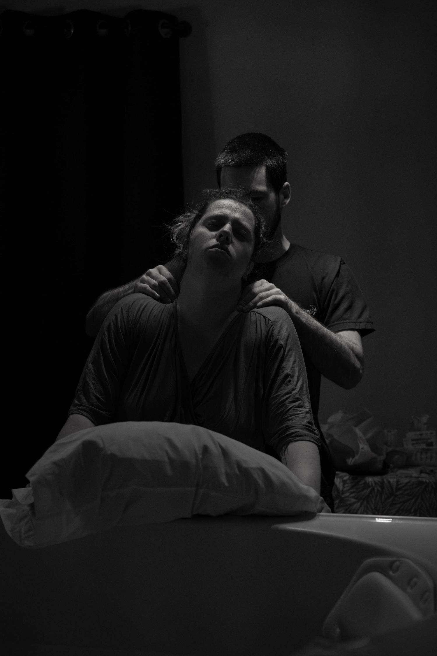 Black and white photo of a man supporting a woman during labor at home.