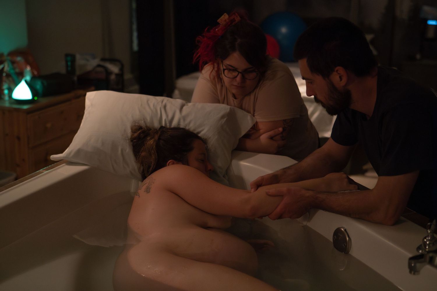 Woman laboring in a birthing tub supported by a midwife and partner at home.