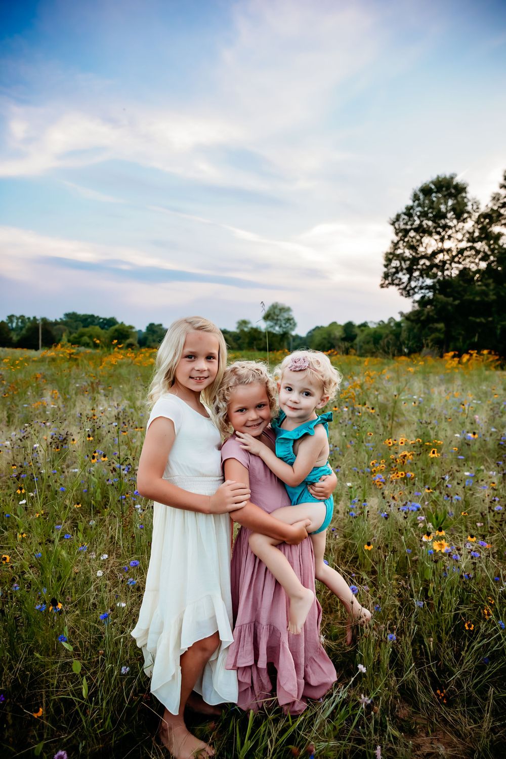 Three children embrace while standing in a wildflower meadow during golden hour.