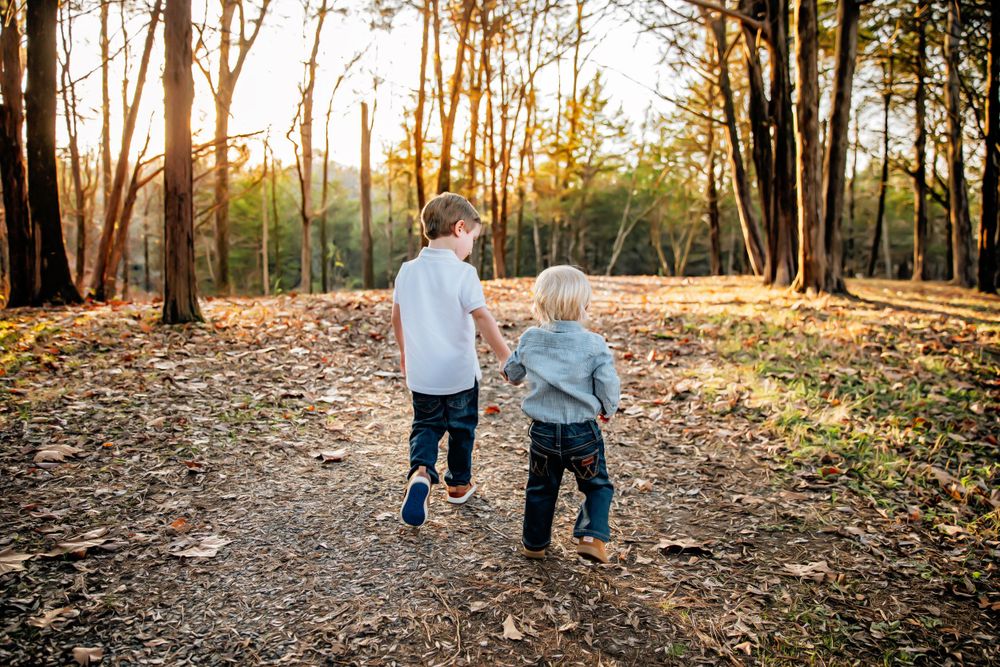Two people running together on leaf-covered trail in sunlit forest.