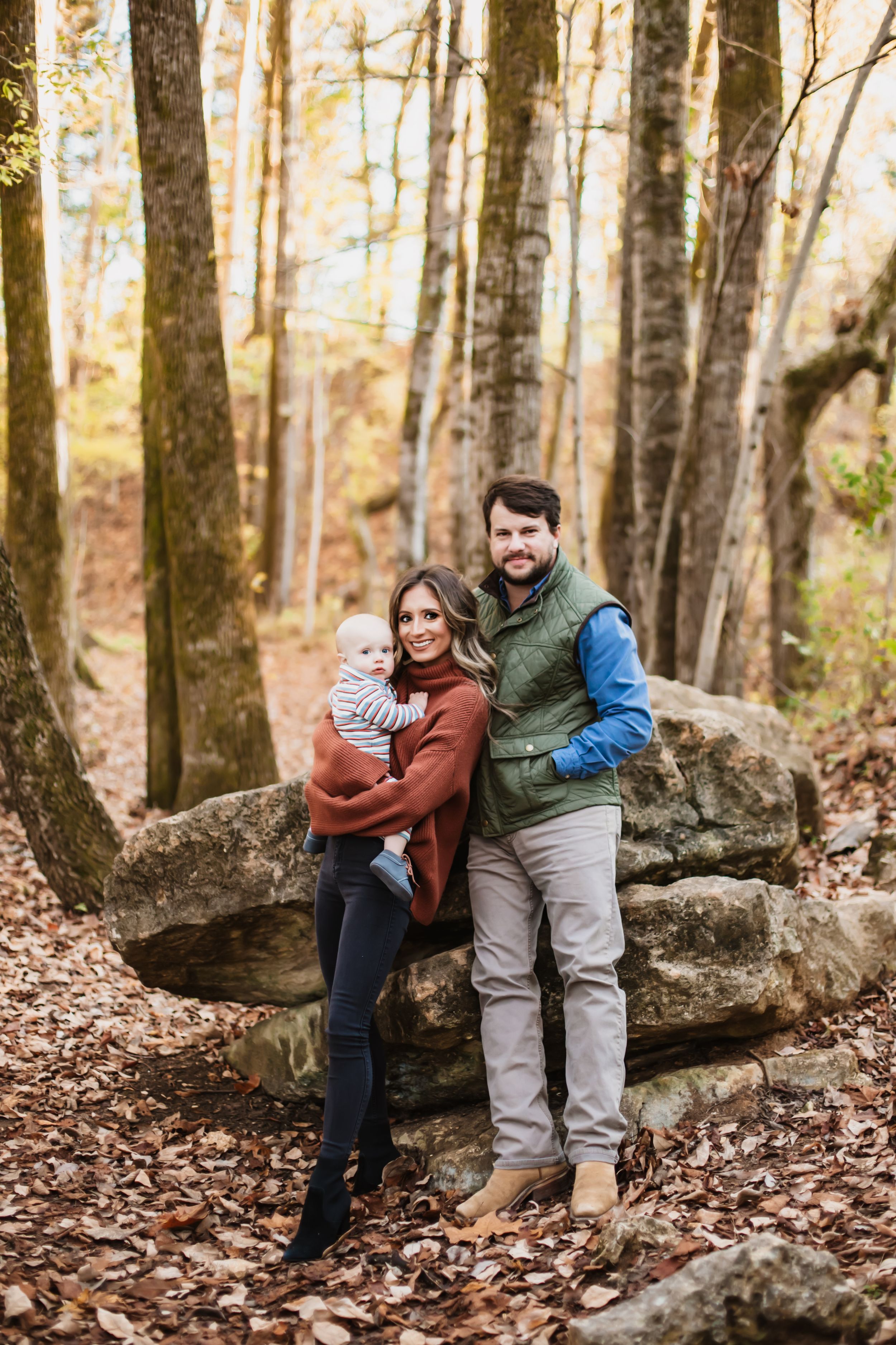 Family of three posing on large rocks in autumn forest setting.
