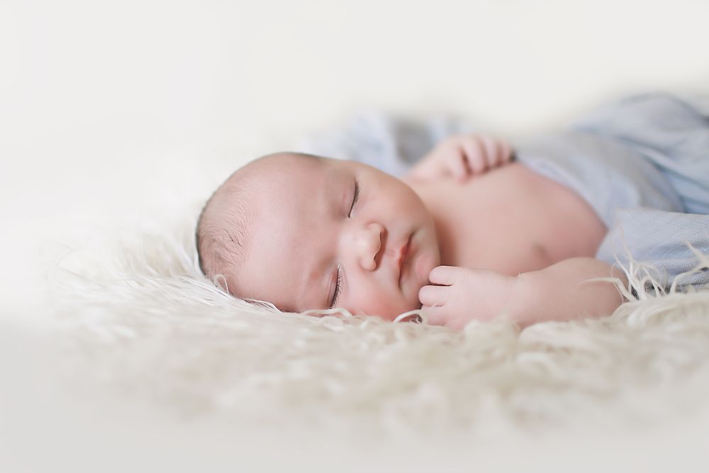 Peaceful sleeping newborn baby on soft white furry blanket.