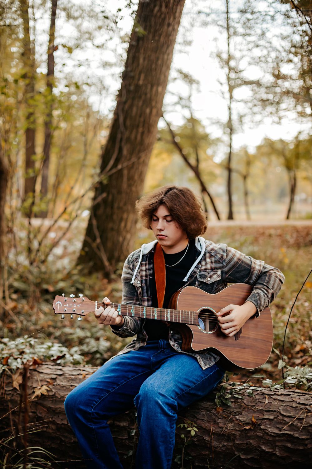 Artistic portrait of someone playing acoustic guitar in an autumn forest setting.