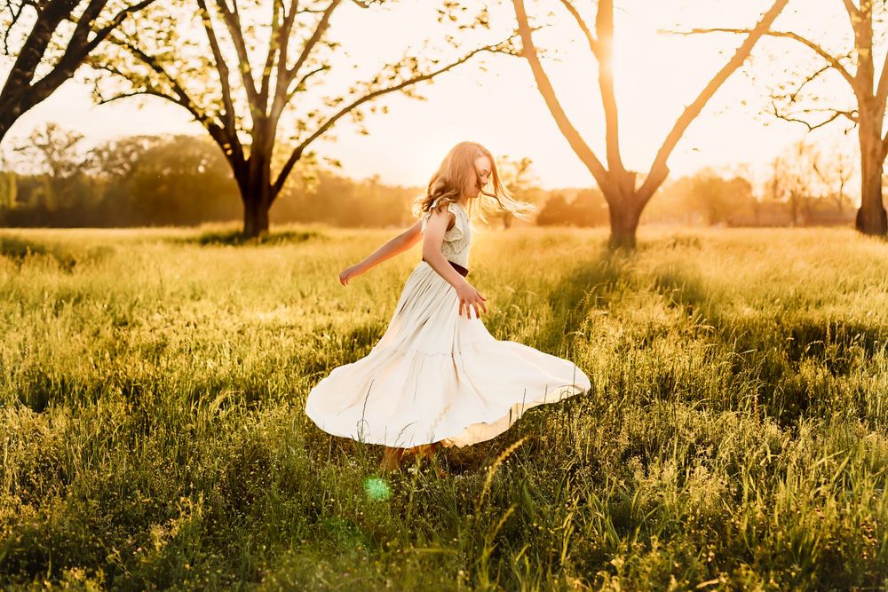 Woman in white dress twirling in sunlit meadow at golden hour.