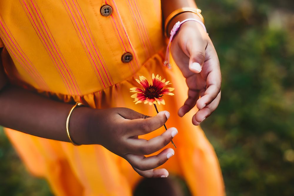 Hands hold a vibrant orange flower against a matching orange dress.