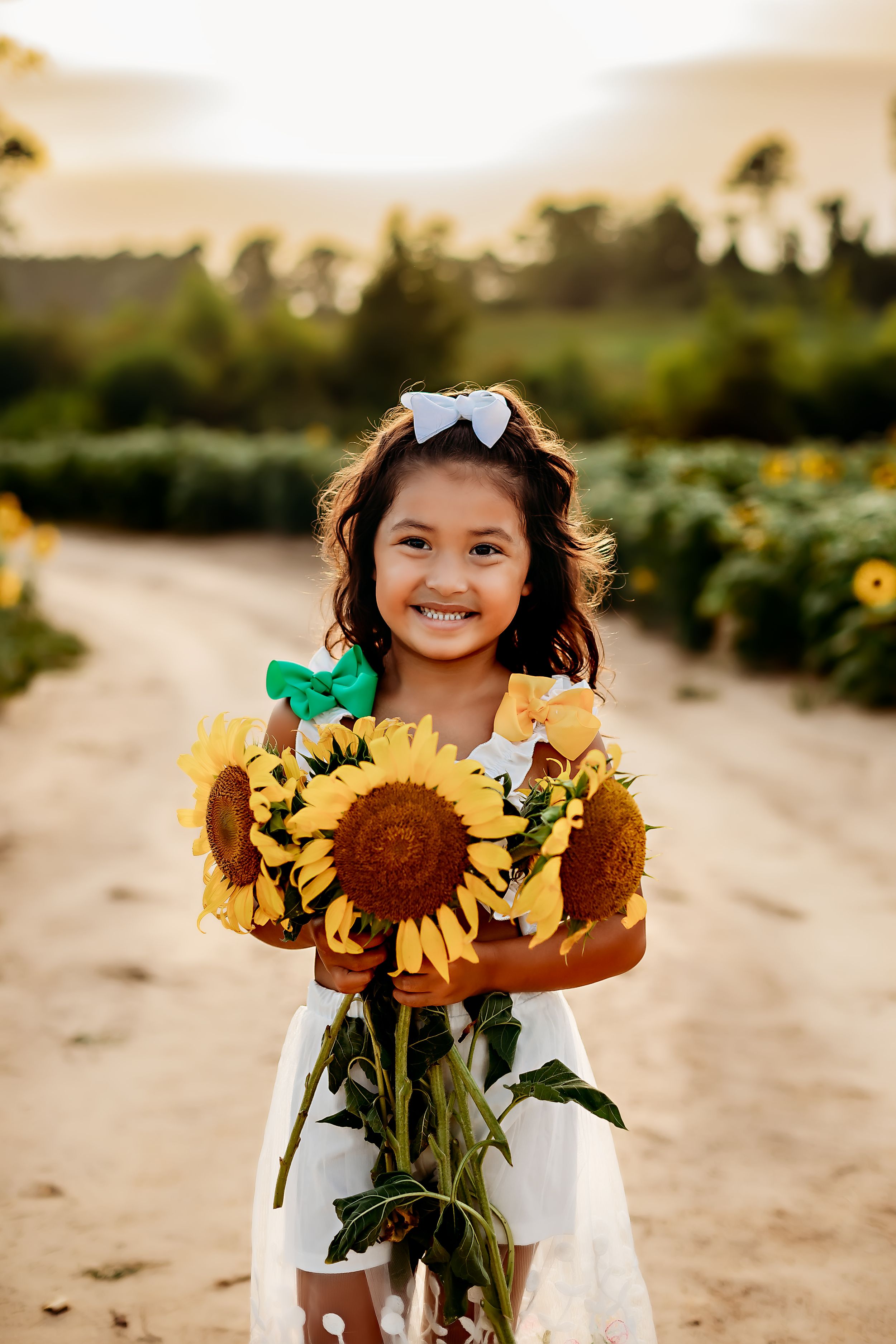 Young girl holding bouquet of sunflowers on dirt path at sunset.