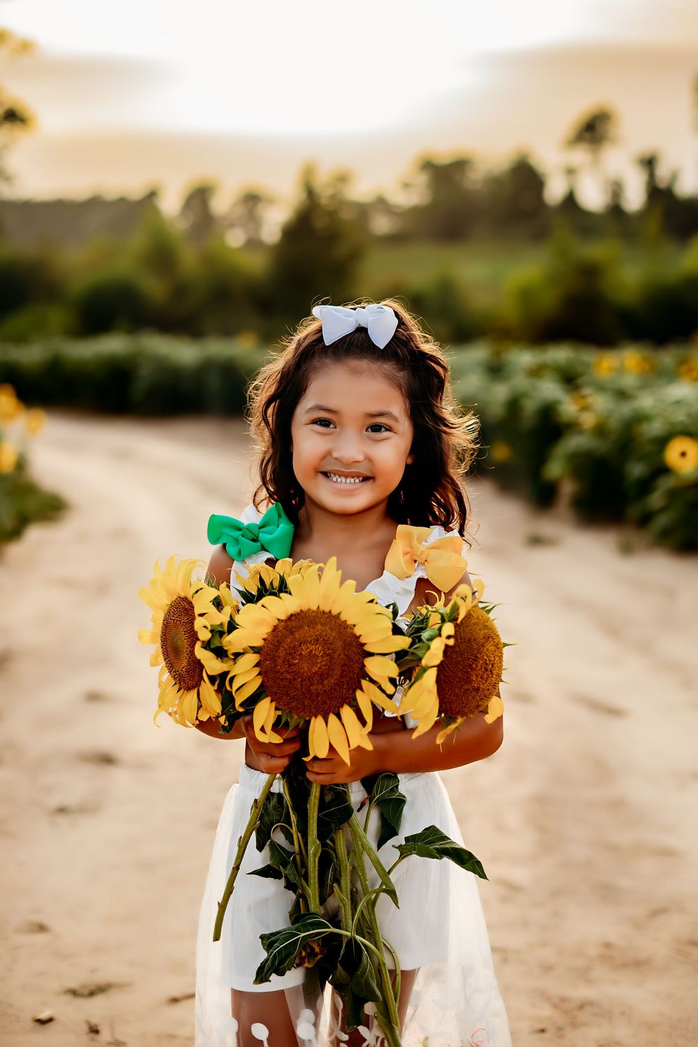 Young girl holding bouquet of sunflowers on dirt path at sunset.