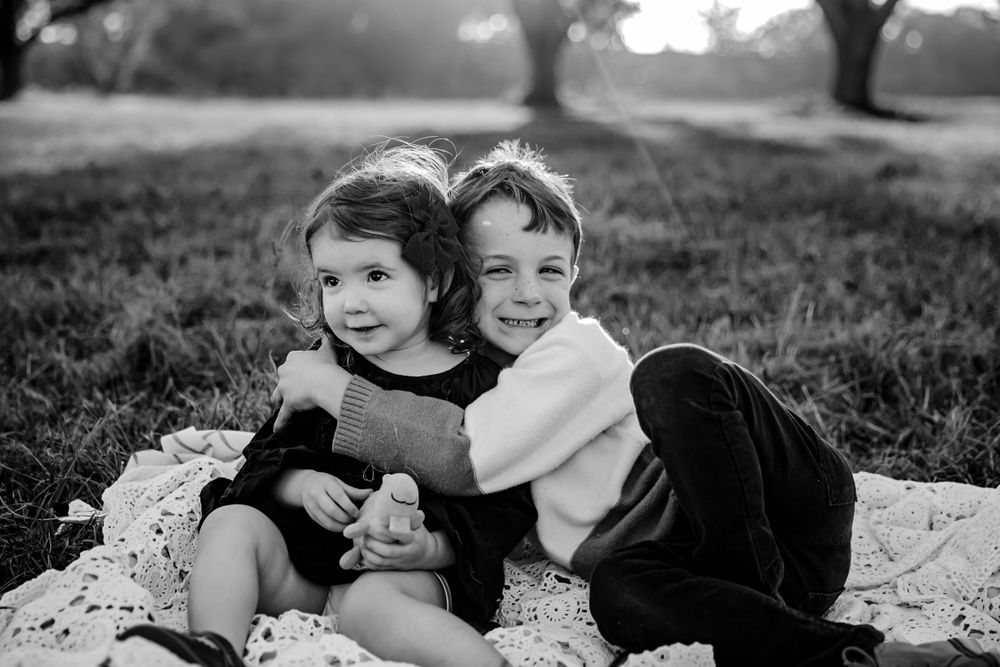 Black and white photo of two children embracing on a blanket outdoors.