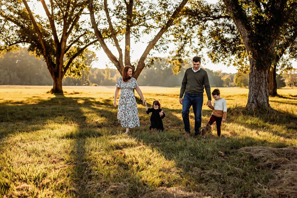 Family walking together at sunset through a golden field with large trees.