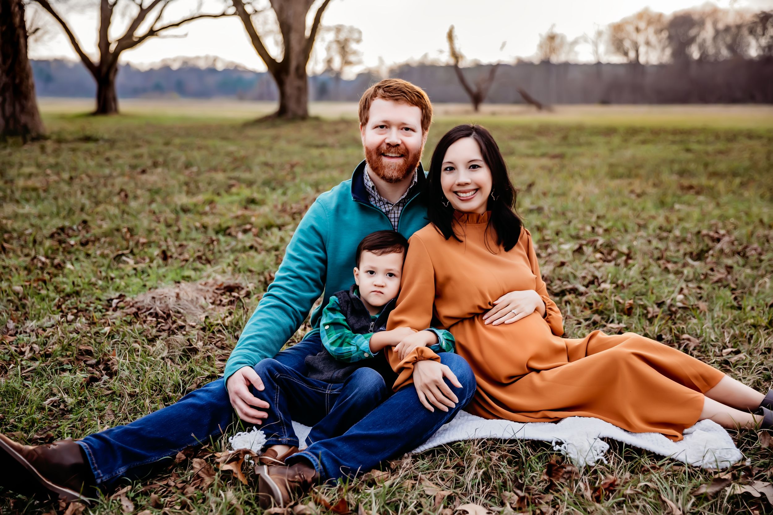 Family relaxing together on blanket in field during golden hour.