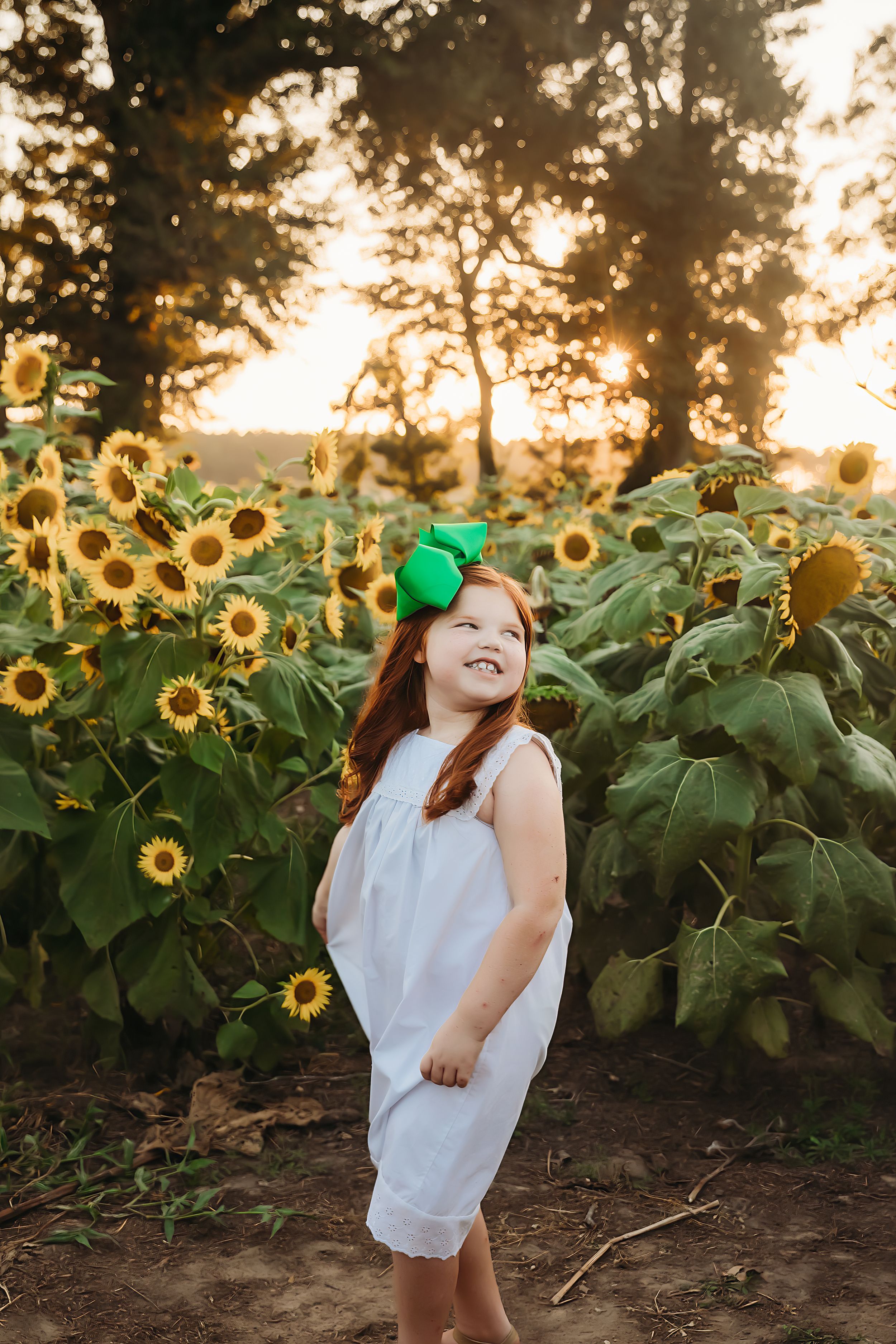 Young girl in white dress joyfully poses in a sunflower field at sunset.