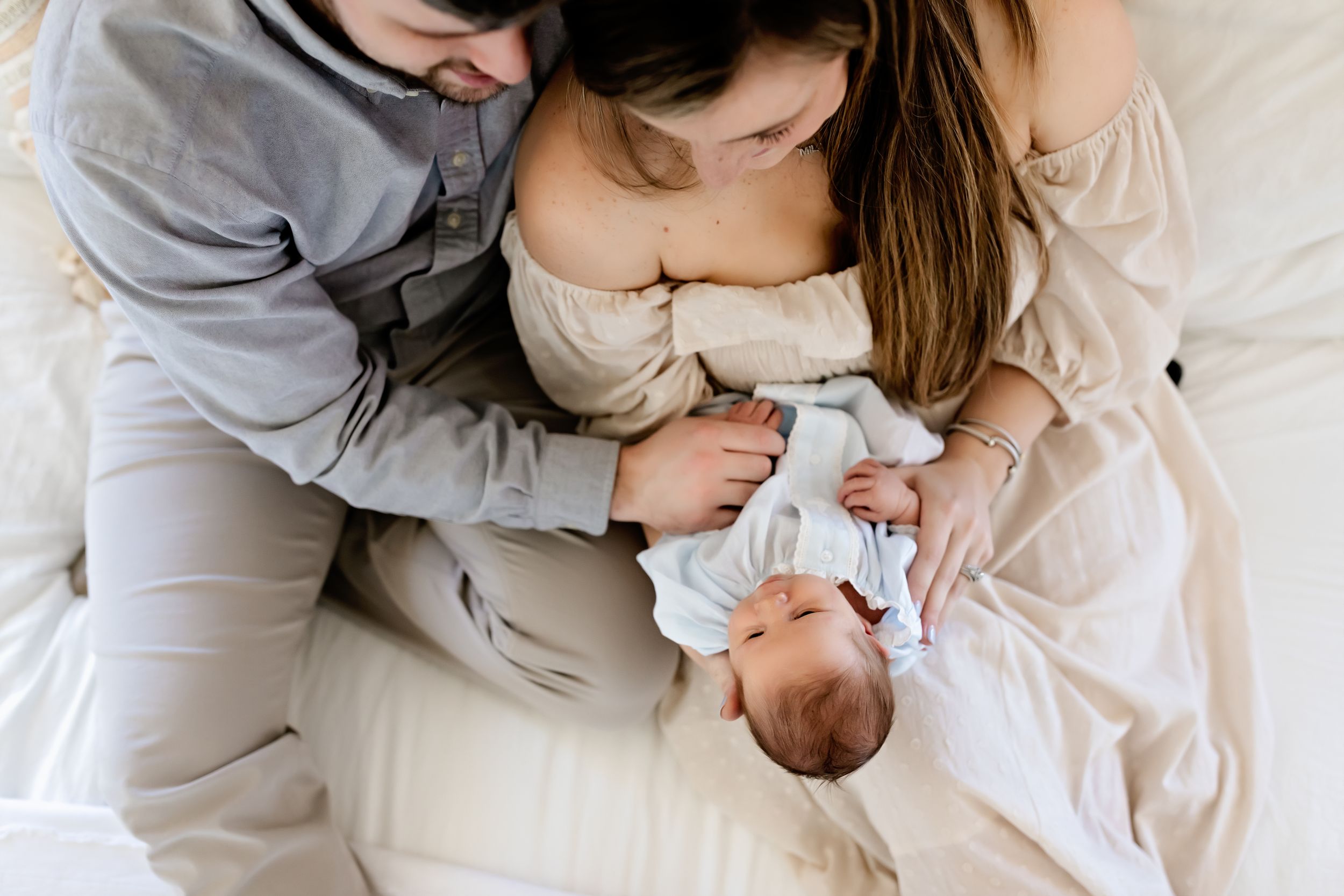 Parents cuddling with newborn baby in soft natural light setting.