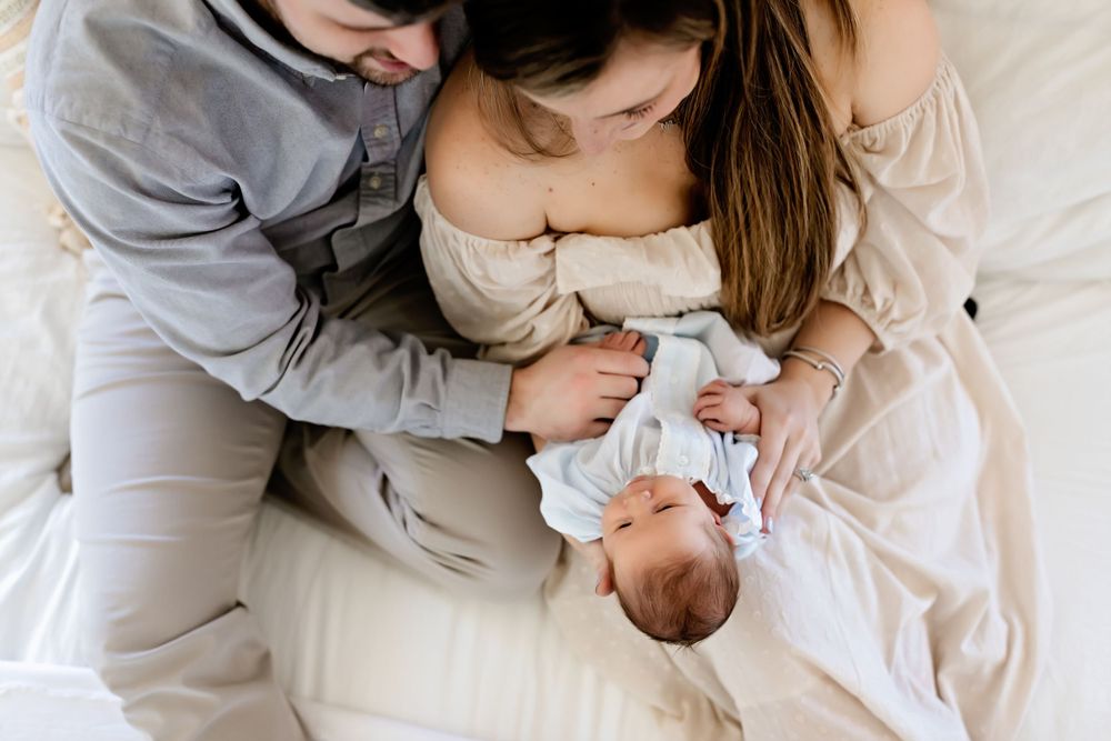 Parents cuddling with newborn baby in soft natural light setting.