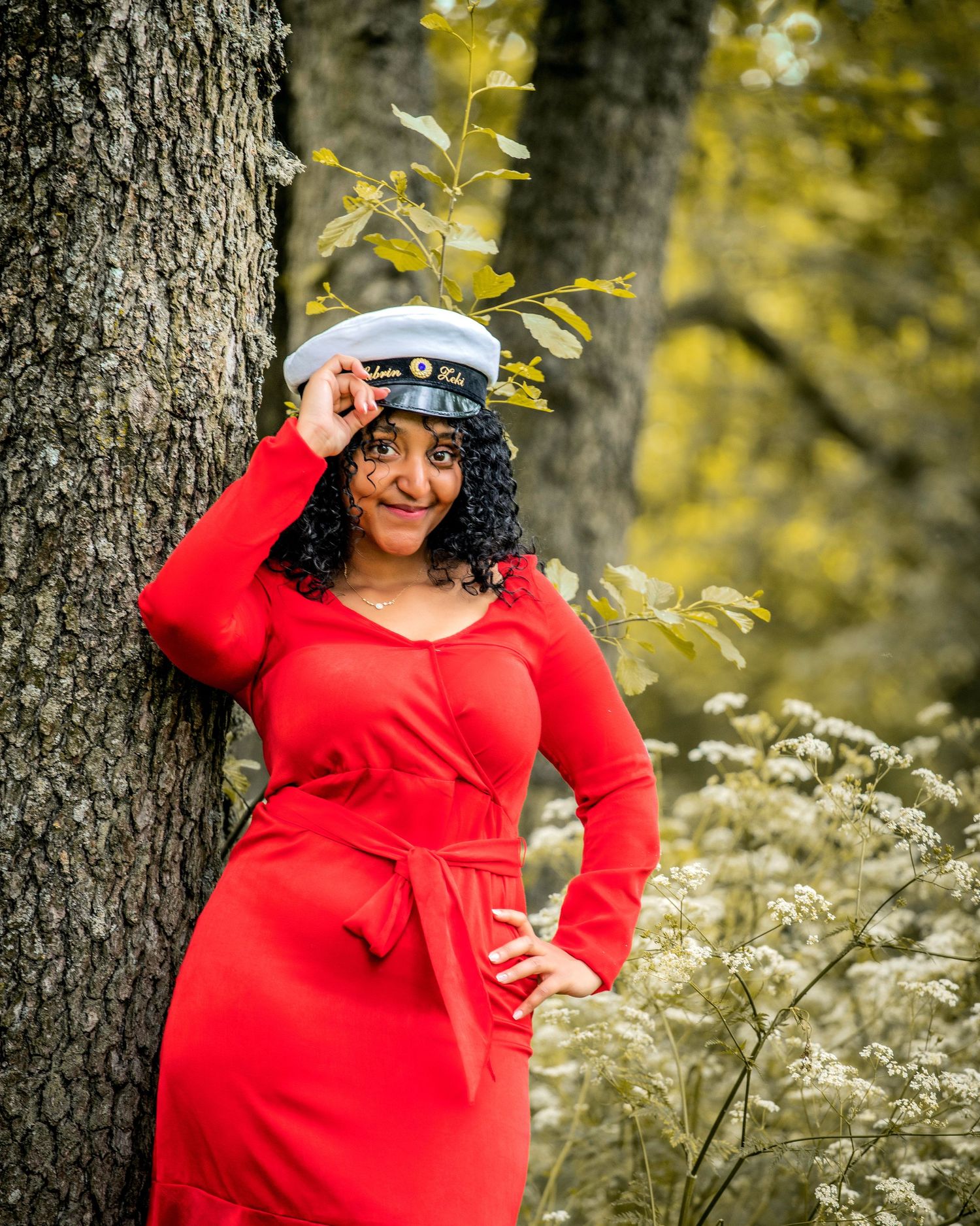 Portrait of woman in red dress posing by tree trunk in autumn setting.