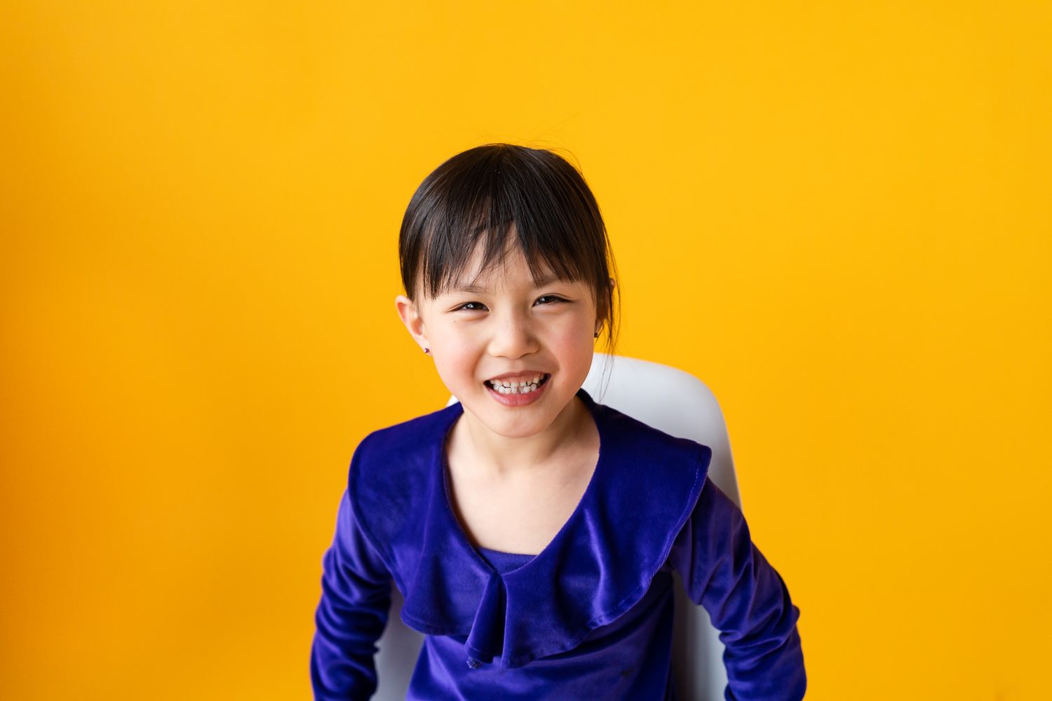 Portrait of a smiling girl wearing a purple shirt in front of a yellow backdrop at North City Studio