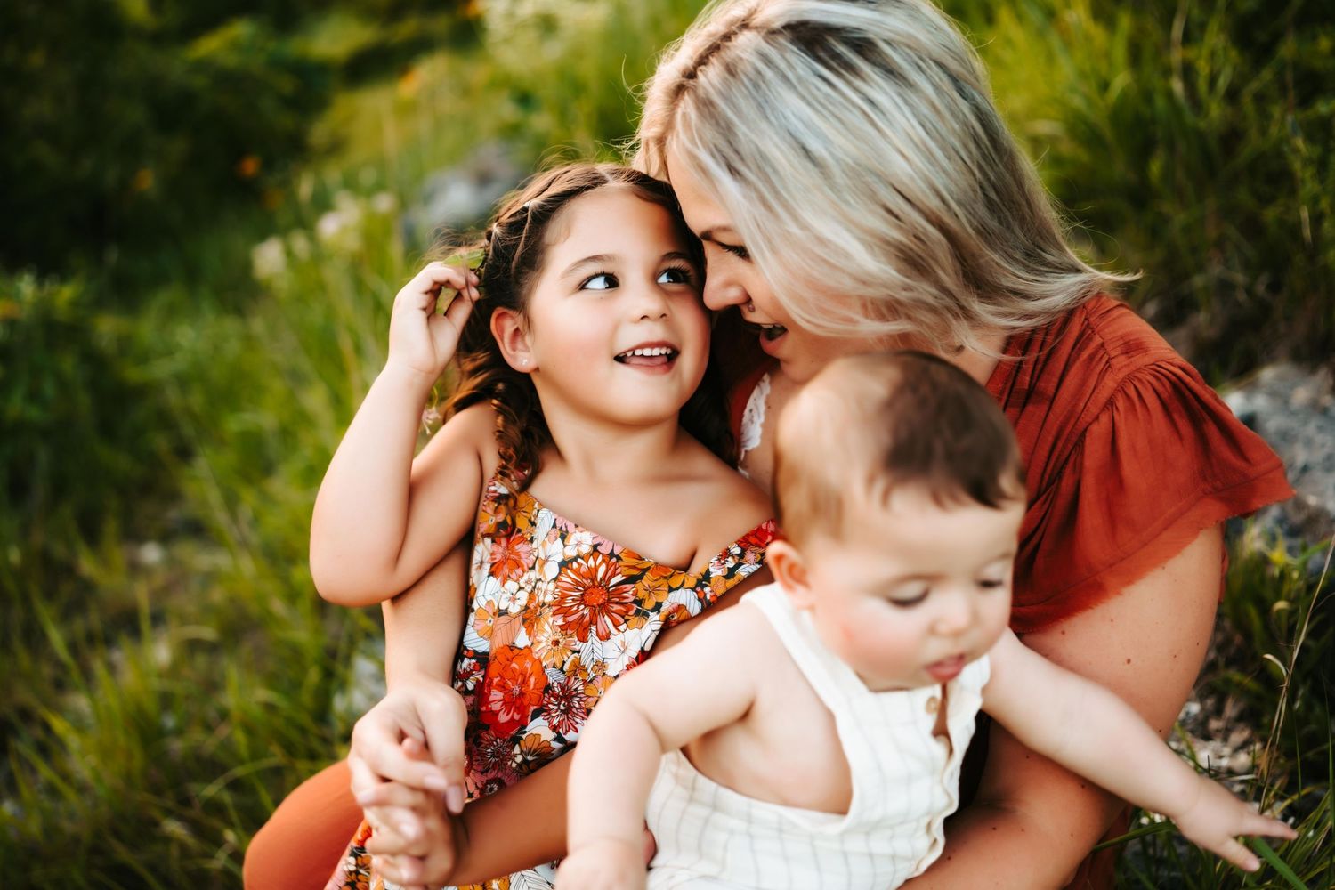A tender outdoor family moment captured in natural lighting with vibrant orange and red clothing.