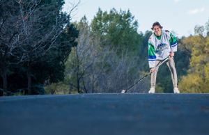 Person in athletic stance on dark surface with trees in background.
