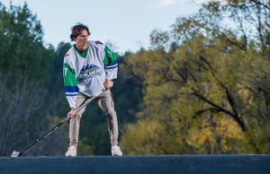 Figure in vintage hockey jersey poses dramatically on outdoor surface against autumn trees.