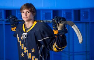 Hockey player poses in yellow and black uniform against blue locker room background.