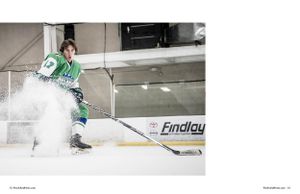 Hockey player in green jersey sprays ice while stopping on indoor rink with Findley banner in background.