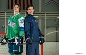 Hockey player in green jersey and coach in blue jacket stand on ice rink.