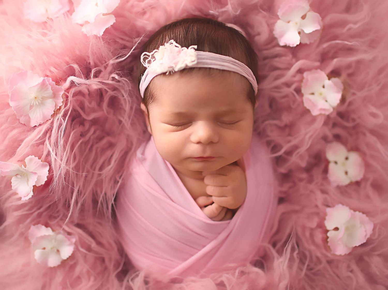 Baby girl in a pink wrap laying on pink fur with pink fur surrounding her. affordable newborn photography Houston